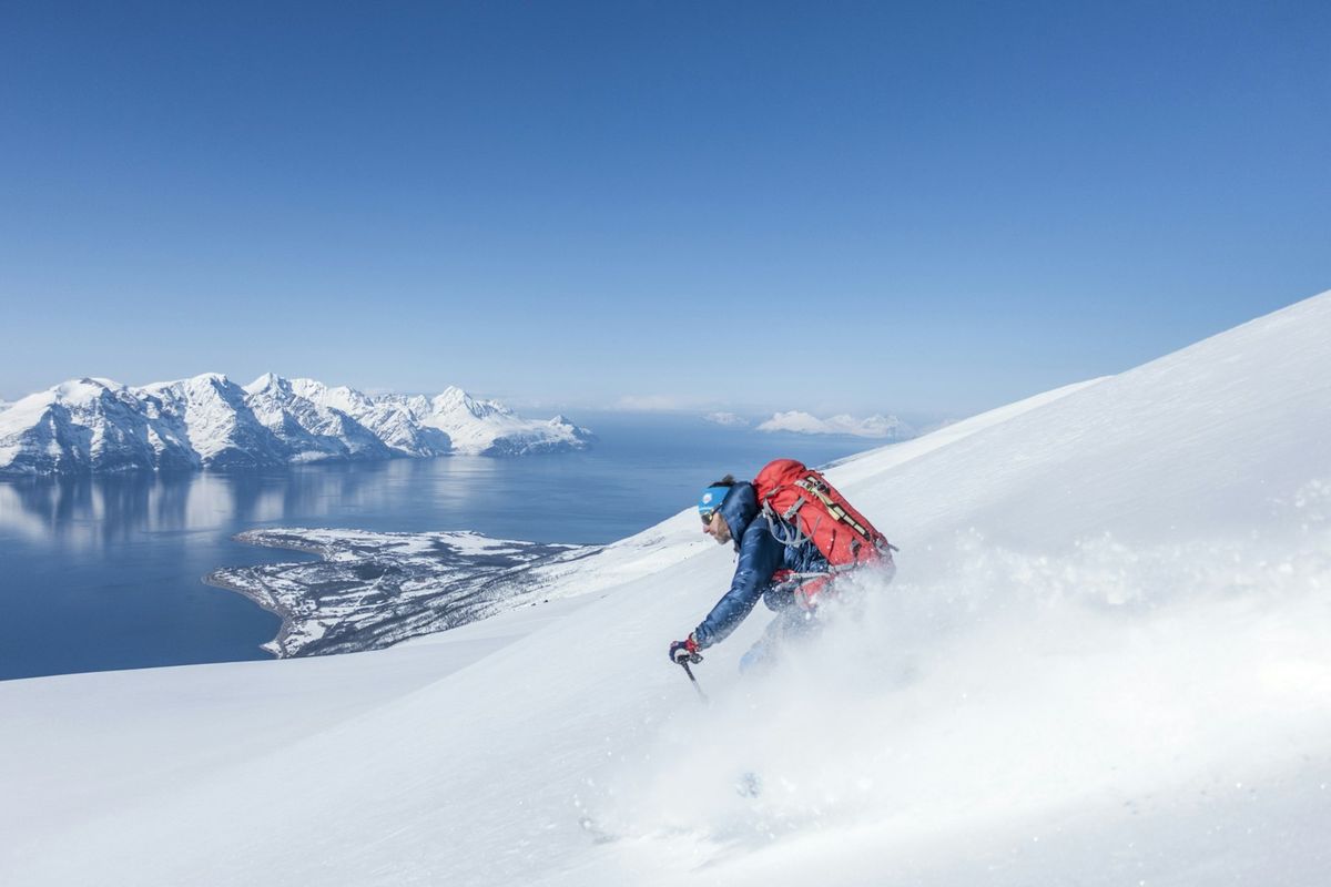 Toppturskiløper kjører ned snødekt fjellside over en fjord
