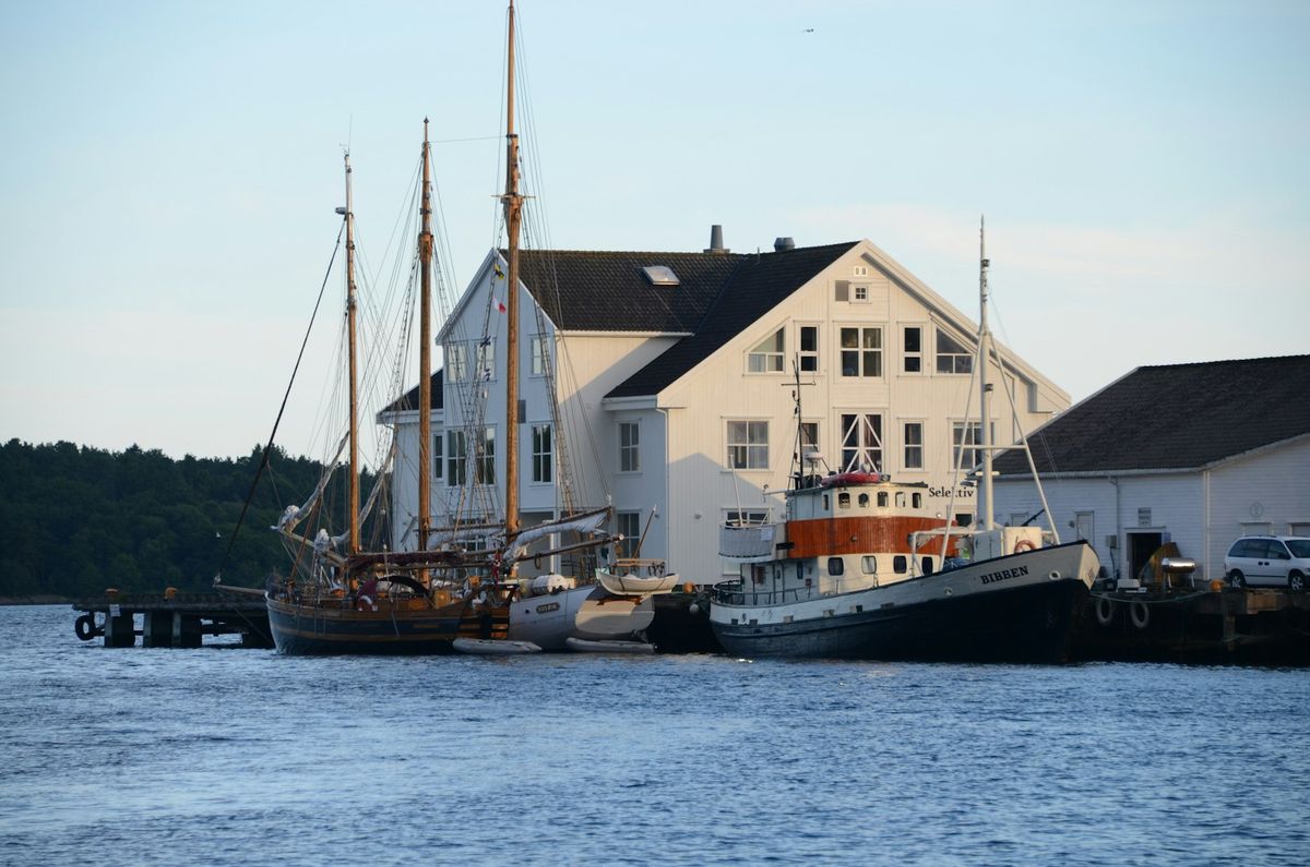Havn på Sørlandet med hvite trehus og båter ved kaia