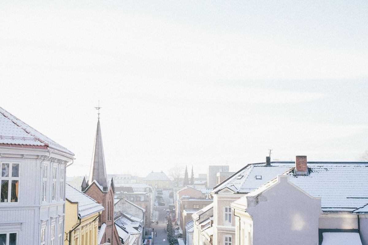 Snødekt utsikt over hustak, kirkespir og en gate i en norsk by om vinteren
